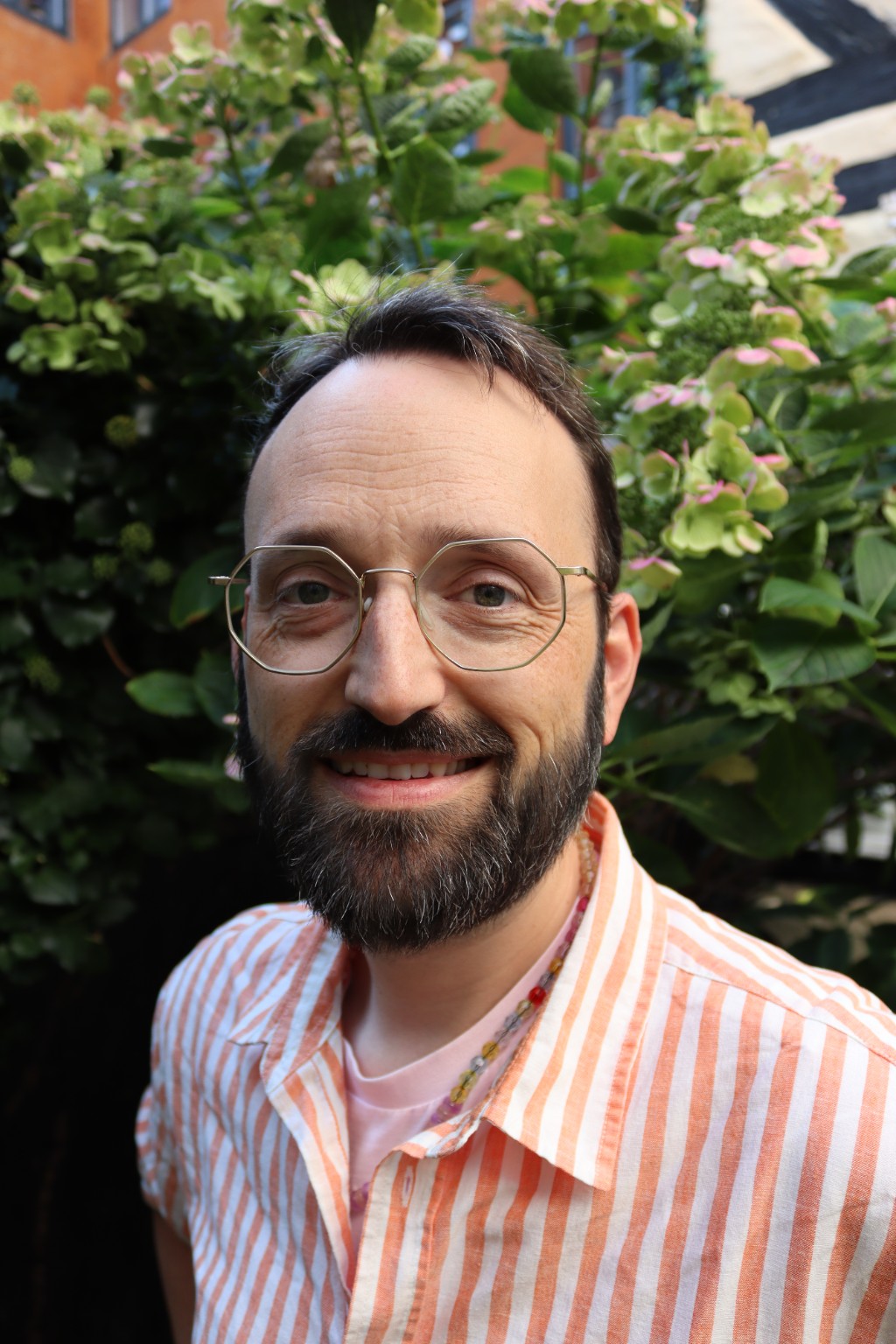 Andreas Busk smiling in front of green flowering plants